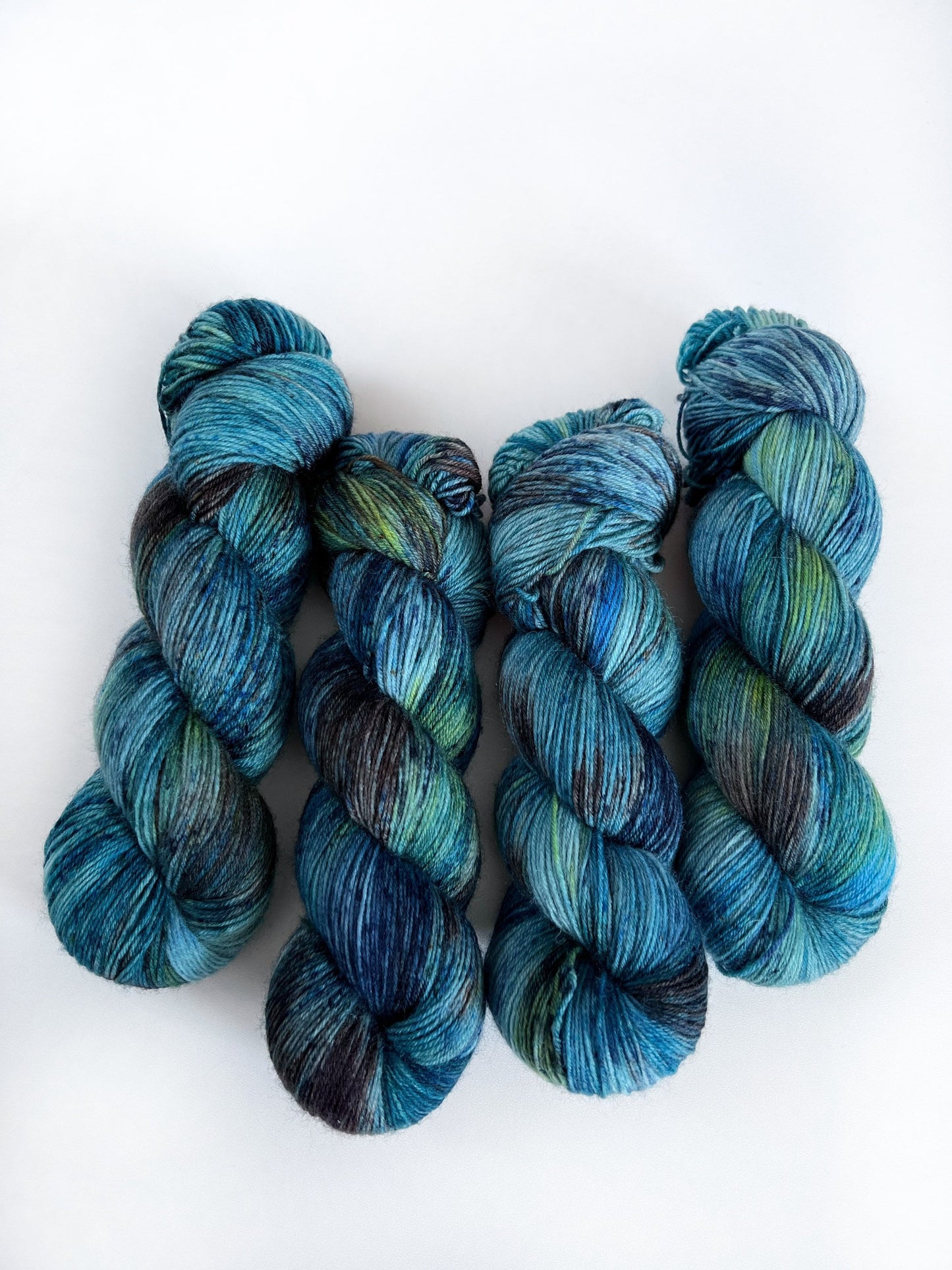 May include: Four skeins of yarn in shades of blue, green, and black. The yarn is hand-dyed and has a variegated color pattern.